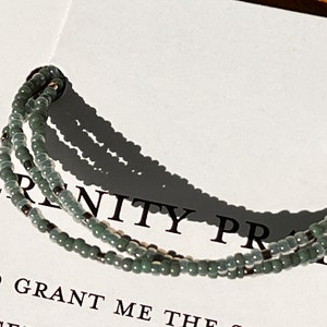 May include: A triple-strand bracelet made of small, light green beads with silver accents. The bracelet is on a white background with the text "Serenity Prayer" and "God grant me the" visible.