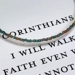 May include: A teal and gold beaded bracelet with the text "2 Corinthians 5:7 I will walk by faith even when I cannot see" on a white background.