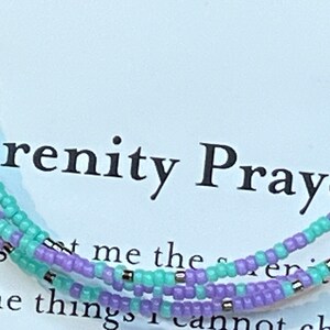 May include: A triple-strand beaded bracelet with lavender and turquoise beads and silver accents. The bracelet is on a white card with the text "Serenity Prayer".