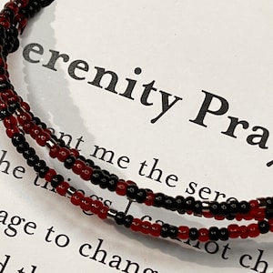 May include: A red and black beaded bracelet with the text "Serenity Prayer" on a white background.
