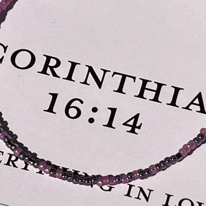 May include: A purple and silver beaded bracelet with the text "CORINTHIANS 16:14" on a white background.