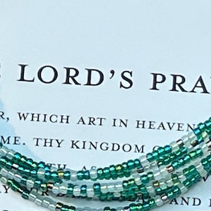 May include: A multi-strand beaded bracelet with green and white beads. The bracelet is on a white background with the text "HE LORD'S PRAY" and part of the Lord's Prayer.