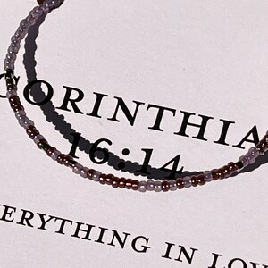 May include: A beaded bracelet with purple and brown beads. The bracelet has the text "1 Corinthians 16:14" and "Everything in Love" on it.