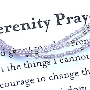 May include: A delicate, layered bracelet composed of small, light purple beads and silver-toned accents. The bracelet is set against a white background with the text "Serenity Prayer" and other text.