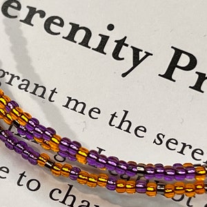 May include: A close-up of a purple and gold beaded bracelet with the text "Serenity Prayer" and "grant me the seren" visible in the background.