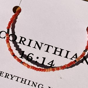 May include: A red and white beaded bracelet with black beads and the text "1 Corinthians 16:14" and "Everything" on a white background.
