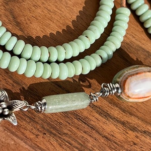 May include: A green stone beaded necklace with a silver flower charm and a large oval agate pendant.