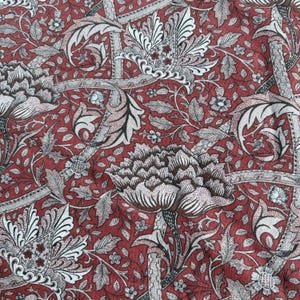 Peut inclure: Gros plan sur un tissu avec un motif floral répété. Le fond est rouge foncé, avec de grandes fleurs et feuilles stylisées en blanc, gris et noir. Le motif a un aspect vintage et botanique.