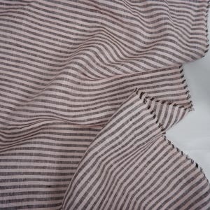 May include: Pink and brown striped linen fabric with a raw edge. The fabric is folded and draped, showing the texture of the linen.