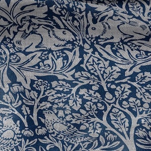 May include: A textile featuring a repeating pattern of rabbits, birds, and foliage in blue and white. The design showcases detailed illustrations of animals and plants, creating a nature-inspired aesthetic.
