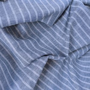 May include: Blue and white striped fabric with a textured weave. The fabric is folded and draped, showing the pattern and texture.
