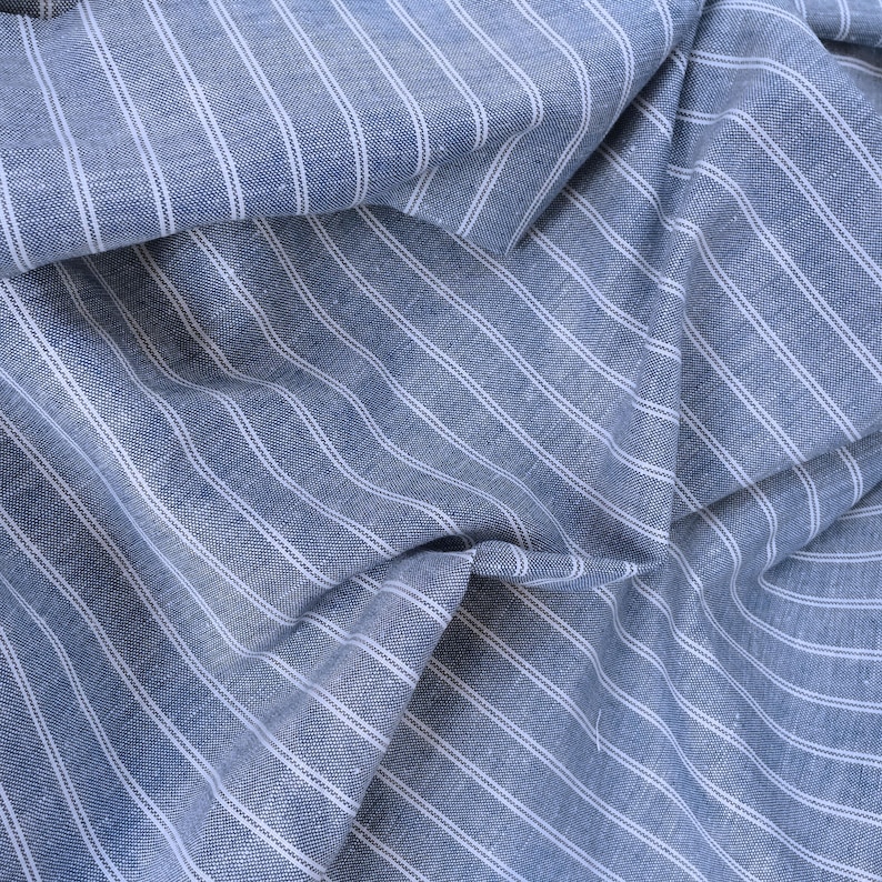 May include: Blue and white striped fabric with a textured weave. The fabric is folded and draped, showing the pattern and texture.