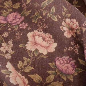 May include: A brown fabric with a floral pattern. The flowers are pink and white with green leaves.
