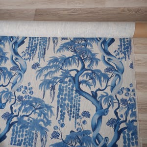 May include: A roll of fabric with a blue and white tree pattern. The design showcases stylized trees with twisting trunks, leafy branches, and hanging flower clusters. The fabric has a light background, and the trees are a vivid blue.