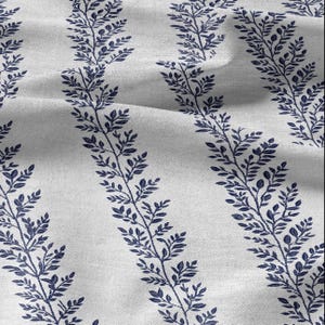 May include: A close-up of white fabric featuring a repeating pattern of navy blue leafy vines. The vines are arranged vertically, creating a striped design. The fabric has a slightly textured appearance, with subtle folds and shadows adding depth.