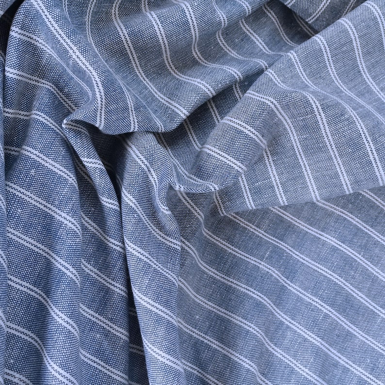 May include: Blue and white striped fabric with a textured weave. The fabric is folded and draped, showing the diagonal stripes.