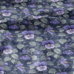 Könnte beinhalten: Ein Stoff mit einem sich wiederholenden Blumenmuster. Das Design zeigt lila Stiefmütterchen mit gelben Zentren und grünen Blättern auf einem dunkelblauen Hintergrund. Der Stoff hat ein leicht strukturiertes Aussehen.