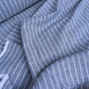 May include: Blue and white striped fabric with a subtle texture. The fabric is folded and draped, showing the pattern and weave.