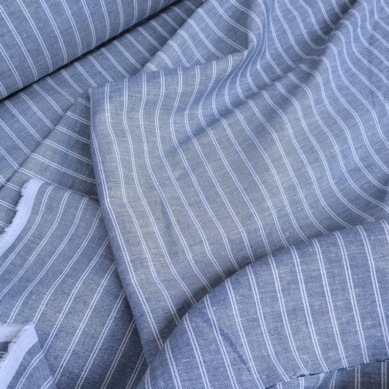 May include: Blue and white striped fabric with a subtle texture. The fabric is folded and draped, showing the pattern and weave.