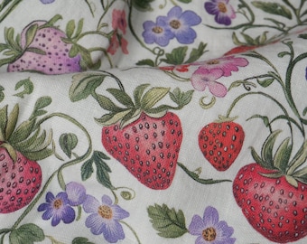 May include: A close-up of a white fabric featuring a repeating pattern of red strawberries, purple and pink flowers, and green leaves. The fabric has a vintage botanical design with a slightly textured appearance.