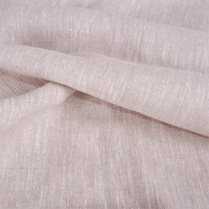 May include: Close-up of a light beige linen fabric with a textured weave. The fabric is folded and draped, showing the natural wrinkles and folds.