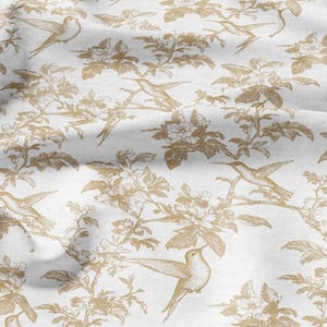 Peut inclure: Tissu blanc avec un motif répété de colibris et de branches fleuries de couleur or. Le motif présente des illustrations détaillées d'oiseaux en vol et perchés sur des branches, créant une esthétique classique et élégante.