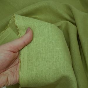 May include: A close-up of a light green linen fabric. The fabric has a slightly textured surface and is folded in a way that shows the weave of the material.