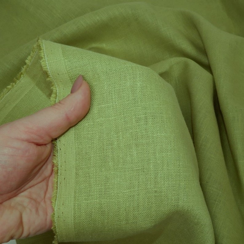May include: A close-up of a light green linen fabric. The fabric has a slightly textured surface and is folded in a way that shows the weave of the material.