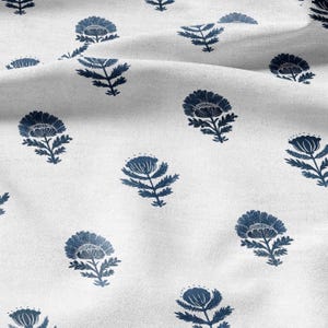 May include: White fabric featuring a repeating pattern of navy blue floral motifs. The flowers are intricately designed, with multiple petals and leafy stems. The fabric has a soft, textured appearance, with subtle shadows adding depth to the design.