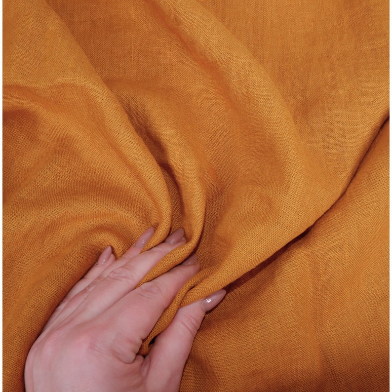 May include: A close-up of a soft, textured, mustard yellow fabric. The fabric is folded and draped, showing its natural wrinkles and texture.
