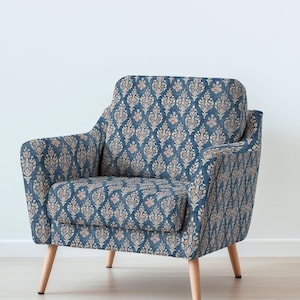 May include: Blue armchair with a floral pattern in pink and beige. The chair has a rounded back and arms, with light-colored wooden legs. The fabric has a textured appearance, and the chair is set against a white background.