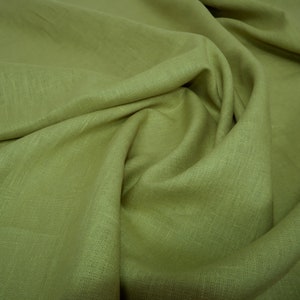 May include: A close-up of a soft, green linen fabric with a textured weave. The fabric is folded and draped, showcasing its natural texture and drape.