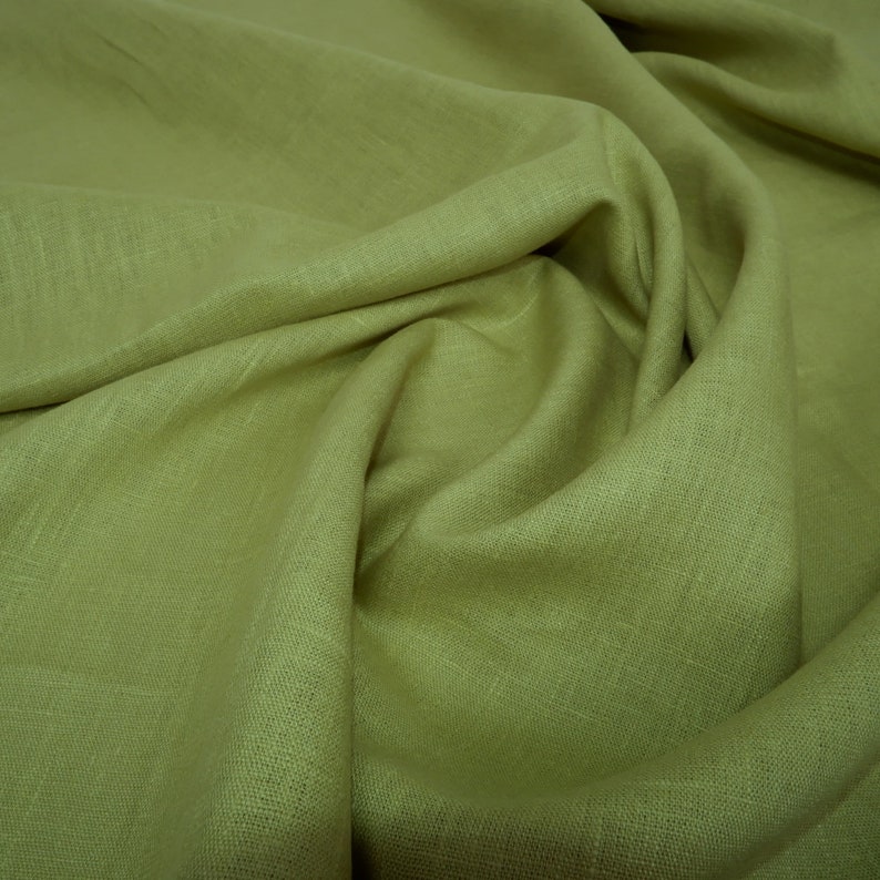 May include: A close-up of a soft, green linen fabric with a textured weave. The fabric is folded and draped, showcasing its natural texture and drape.