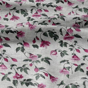 May include: A textile with a floral design. The pattern shows pink flowers with green leaves and stems on a light grey backdrop. The flowers are in different stages of bloom, creating a natural, botanical theme.