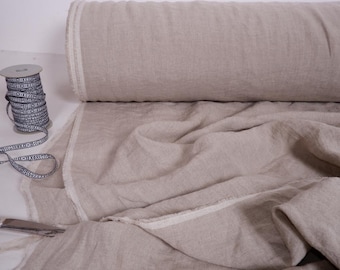 Puede incluir: Un rollo de tela de lino natural con un borde blanco. La tela está doblada y drapeada sobre una mesa. Un carrete de cinta blanco y negro está en primer plano.
