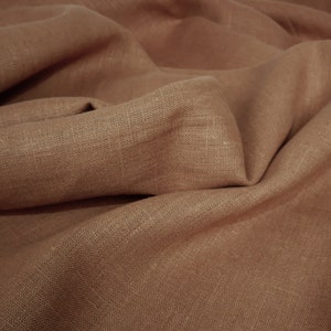 May include: Close-up of a brown linen fabric with a textured weave. The fabric is folded and draped, showing its soft and natural texture.