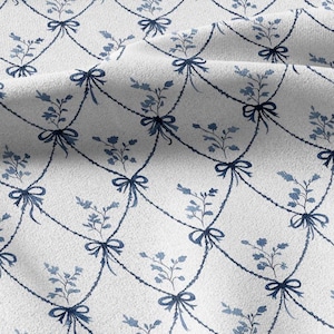 May include: A white fabric featuring a repeating pattern of dark blue rope-like swags arranged in a diamond grid. Each intersection of the rope is adorned with a dark blue bow, and a small blue floral sprig is centered within each diamond shape.