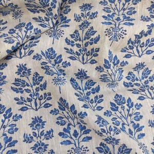 May include: A beige linen fabric with a repeating pattern of blue floral sprigs. The fabric has a subtle texture and a slightly distressed look.