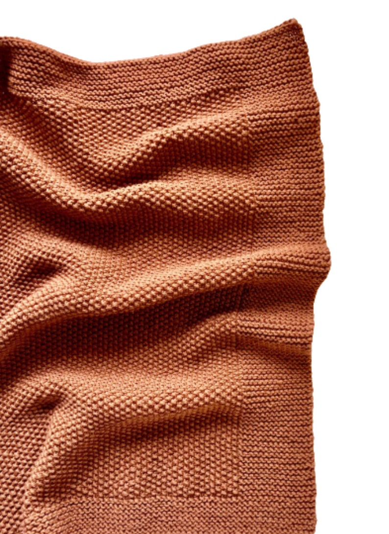 May include: A soft, brown knitted throw blanket with a textured weave. The blanket is folded and draped over a white surface.