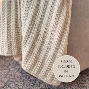 May include: A close-up of a beige knitted throw blanket with a ribbed texture. The blanket is draped over a sofa and the edge of the blanket is folded over. The text "5 SIZES INCLUDED IN PATTERN" is on a white circle with a black outline.
