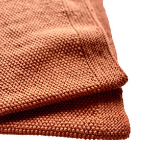 May include: Close-up of a folded terracotta-colored knitted throw blanket with a textured surface.