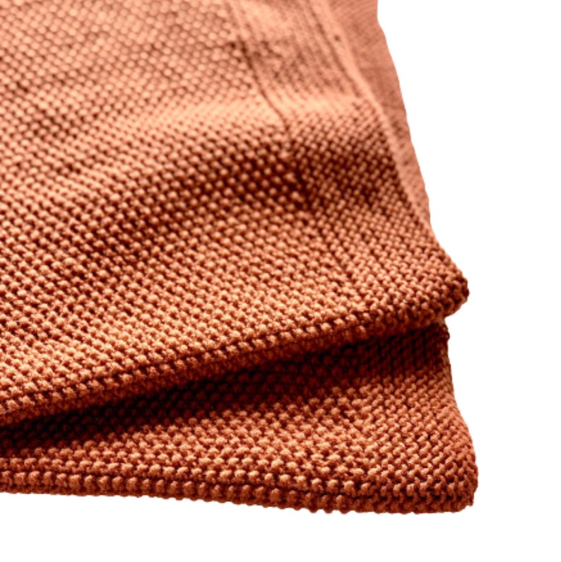 May include: Close-up of a folded terracotta-colored knitted throw blanket with a textured surface.