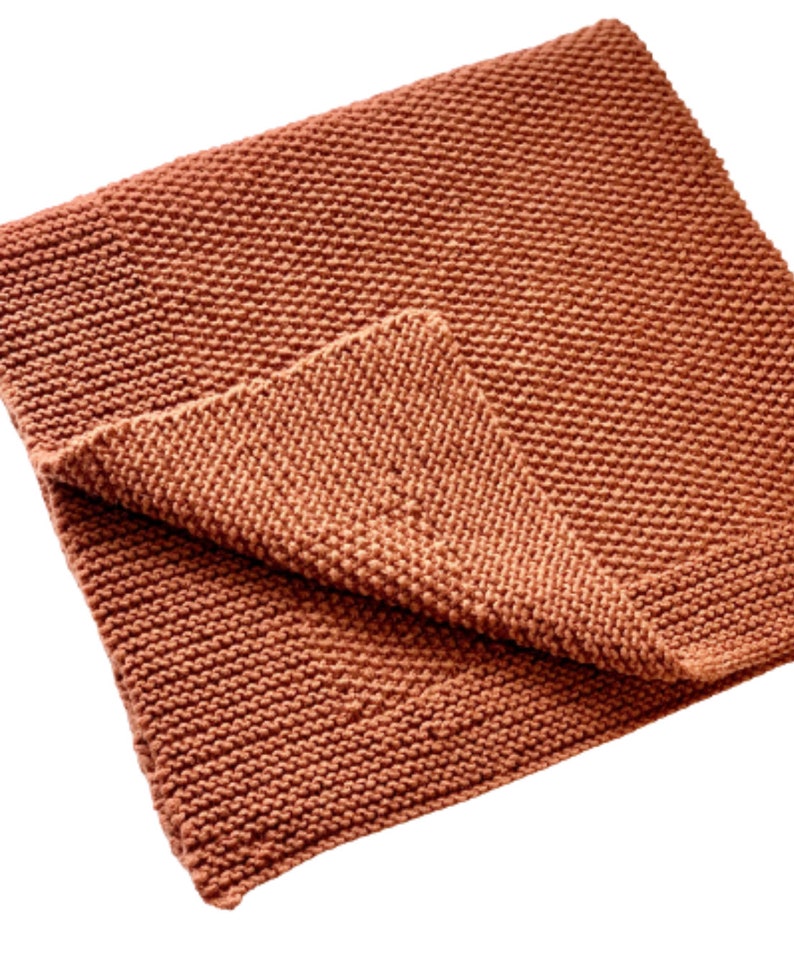 May include: A soft, knitted throw blanket in a warm terracotta color. The blanket is folded in half and has a textured, woven pattern.