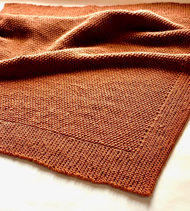 May include: A brown knitted throw blanket with a textured weave. The blanket is folded and draped over a white surface.