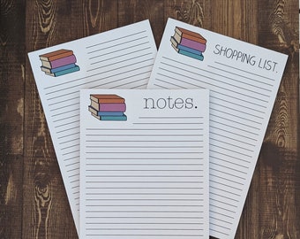 May include: Three white lined notepads with a stack of colorful books illustration. The top notepad says "SHOPPING LIST." The middle notepad says "notes."