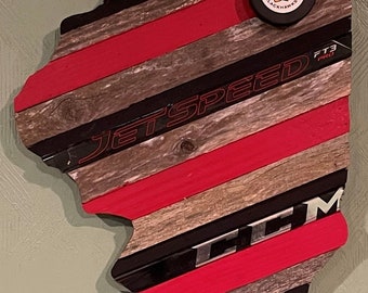 May include: A wooden outline of the state of Illinois, decorated with hockey sticks and a Chicago Blackhawks hockey puck. The sticks are painted red and black, and the words "Jet Speed" and "FT3 Pro" are visible on the sticks.