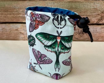 May include: A white drawstring bag with a blue lining and a black drawstring. The bag is printed with a pattern of colorful butterflies and beetles.