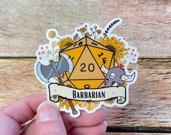 May include: A yellow 20-sided die with a barbarian helmet and axe, surrounded by sunflowers and other flowers. The die has the number 20 on it and the text "BARBARIAN" is on a banner below the die.