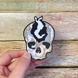 May include: A black and white skull sticker with a blue and white design on the top of the head. The skull has a detailed design with a textured look.