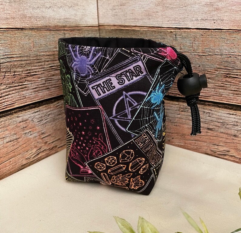 Op de afbeelding: Een zwarte trekkoordtas met een kleurrijk tarotkaartontwerp. De tas heeft verschillende kaarten, waaronder de kaart "The Star".